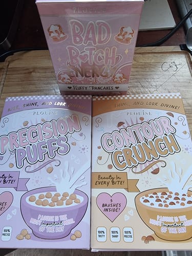 Reviewer's pink 'Bad Bitch Energy Lip Duo' box on a wooden surface with other P.Louise makeup products.