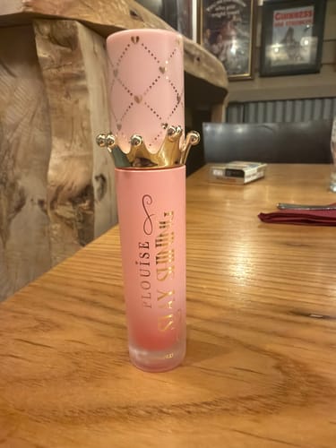 Customer's Bad Bitch Energy Lip Oil in its pink and gold crown packaging, standing on a wooden table.