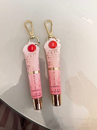 Customer's Bad Bitch Energy Lip Duo tubes with gold keychain clips on a glass table.